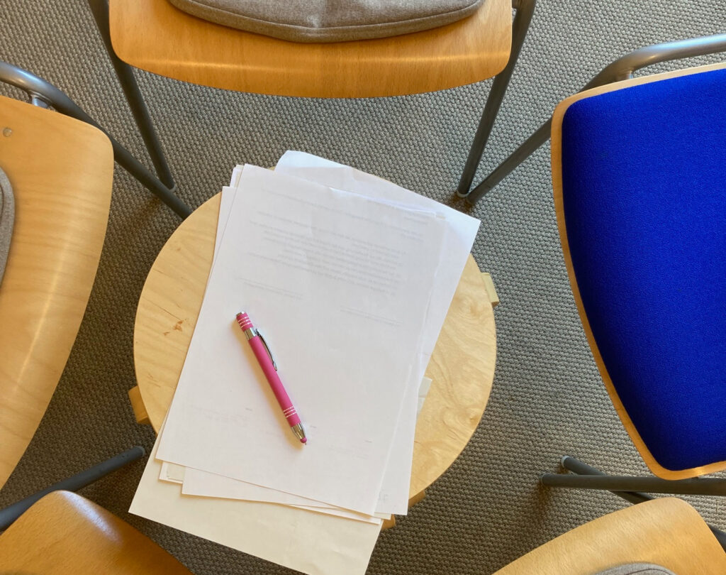 fünf Stühle um ein Tischchen mit Papier und Kugelschreiber